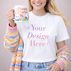 May include: White ceramic mug with a colorful Easter design, held by a person wearing a white t-shirt with the text "Your Design Here". The person is also wearing a colorful sweater.