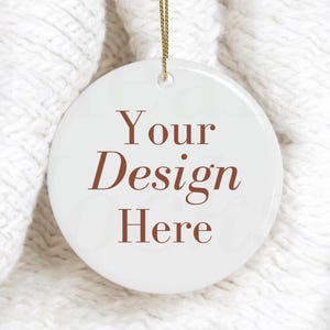 Może przedstawiać: Okrągła biała ceramiczna ozdoba z brązowym napisem Your Design Here nadrukowanym na środku. Ozdoba posiada mały otwór u góry z cienkim złotym sznurkiem do zawieszenia, zapewniając puste miejsce na własne grafiki lub projekty użytkownika.