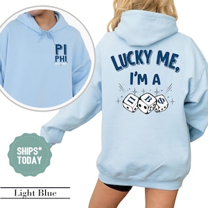 May include: Light blue hooded sweatshirt with the text "Lucky Me, I'm a" and three dice with the letters "Π", "B", and "Φ" on them. The front of the sweatshirt has the text "Pi Phi Est. 1869" in a small pocket.