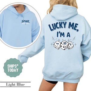 May include: Light blue hoodie with the text "LUCKY ME, I'M A" and dice graphics on the back. The front of the hoodie has the text "DPHIE, EST. 1917". The hoodie is light blue.