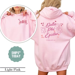 May include: Light pink hooded sweatshirt with a pink Delta Phi Epsilon logo on the back. The logo includes hearts and a lollipop graphic. The front of the sweatshirt has a pink Delta Phi Epsilon logo.