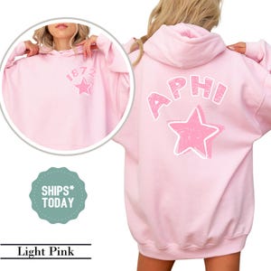 May include: Light pink hoodie with the text "1872" and a star graphic on the front. The back of the hoodie features the letters "APHI" above a star graphic. The hoodie is a light pink color.