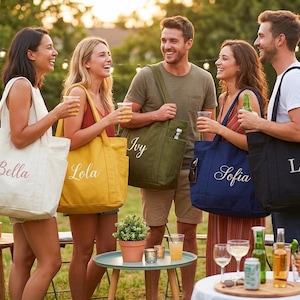 May include: A group of people holding personalized tote bags in various colors, including cream, yellow, olive green, navy blue, and black. Each bag has a name embroidered on it in a cursive font. The scene is outdoors with a blurred background.