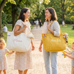 May include: Two women and two children are walking in a park. One woman carries a cream-colored tote bag with "Mama" printed on it. The other woman carries a yellow tote bag with "Mom Life" printed on it. The children are holding hands.