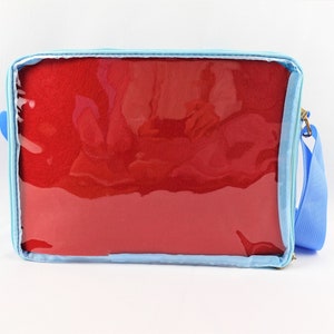 K&ouml;nnte beinhalten: Eine hellblaue Rei&szlig;verschlusstasche mit einem transparenten Plastikfenster. Die Tasche hat ein rotes Stofffutter und einen verstellbaren blauen Schultergurt.
