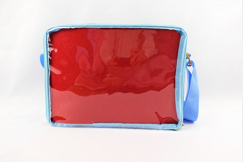 K&ouml;nnte beinhalten: Eine hellblaue Rei&szlig;verschlusstasche mit einem transparenten Plastikfenster. Die Tasche hat ein rotes Stofffutter und einen verstellbaren blauen Schultergurt.