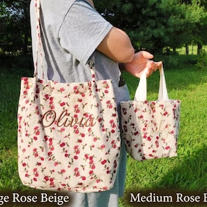 May include: Two beige floral tote bags, one large and one medium, with red rose patterns. The large bag has a shoulder strap and the name "Olivia" embroidered on it. The medium bag has a handle and a name embroidered on it.