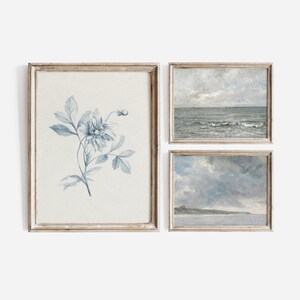 Puede incluir: Conjunto de tres impresiones enmarcadas en un marco de madera clara. Las impresiones son todas en tonos de azul y blanco. Una impresi&oacute;n presenta un dise&ntilde;o floral azul y blanco, otra presenta un paisaje mar&iacute;timo con olas y la tercera presenta un paisaje mar&iacute;timo con un cielo nublado.