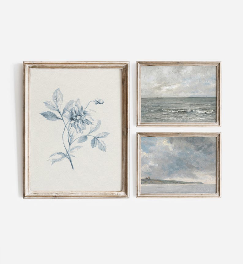 Puede incluir: Conjunto de tres impresiones enmarcadas en un marco de madera clara. Las impresiones son todas en tonos de azul y blanco. Una impresi&oacute;n presenta un dise&ntilde;o floral azul y blanco, otra presenta un paisaje mar&iacute;timo con olas y la tercera presenta un paisaje mar&iacute;timo con un cielo nublado.