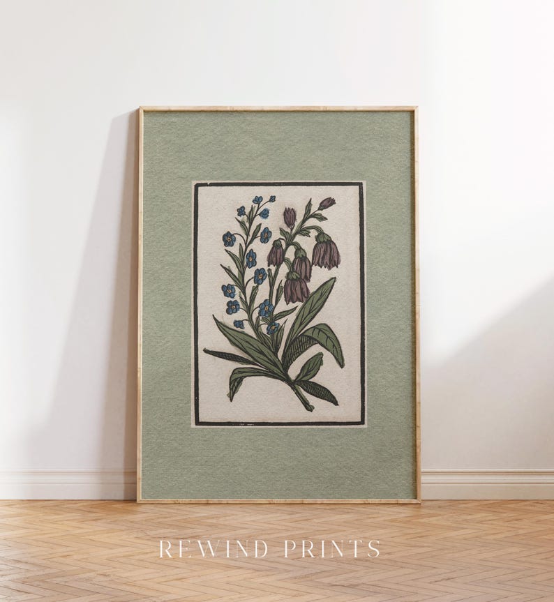 May include: A framed botanical print featuring a detailed illustration of a cluster of purple and blue flowers with green leaves on a cream background. The frame has a sage green mat and a natural wood frame.