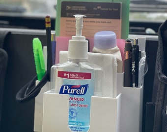 May include: A white plastic organizer with a clear bottle of Purell Advanced Hand Sanitizer. The bottle has a blue label with the text "#1 Brand in Hospitals" and "Most Germs". The organizer is attached to a black car seat.