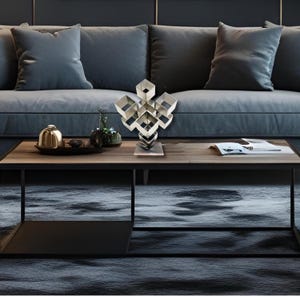 Pode incluir: Uma moderna escultura geométrica prateada com um design de cubo, exibida numa mesa de centro de madeira. A escultura é feita de múltiplas formas quadradas interconectadas. A mesa está em frente a um sofá cinzento.