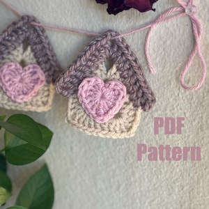 May include: A crochet garland with a pink and brown color scheme featuring a series of small houses with hearts in the center. The garland is strung with pink yarn and the text "PDF Pattern" is visible in the bottom right corner of the image.