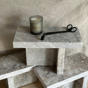 May include: Three stacked gray stone candle holders with a gray candle and a black candle snuffer on the top holder. The candle is labeled "Oakwood"