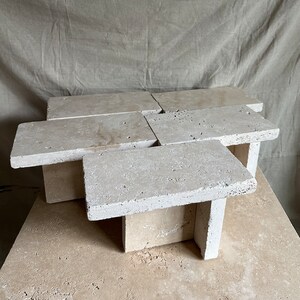 May include: A modern coffee table made of multiple pieces of travertine stone. The table has a unique, geometric design and a natural, earthy finish.