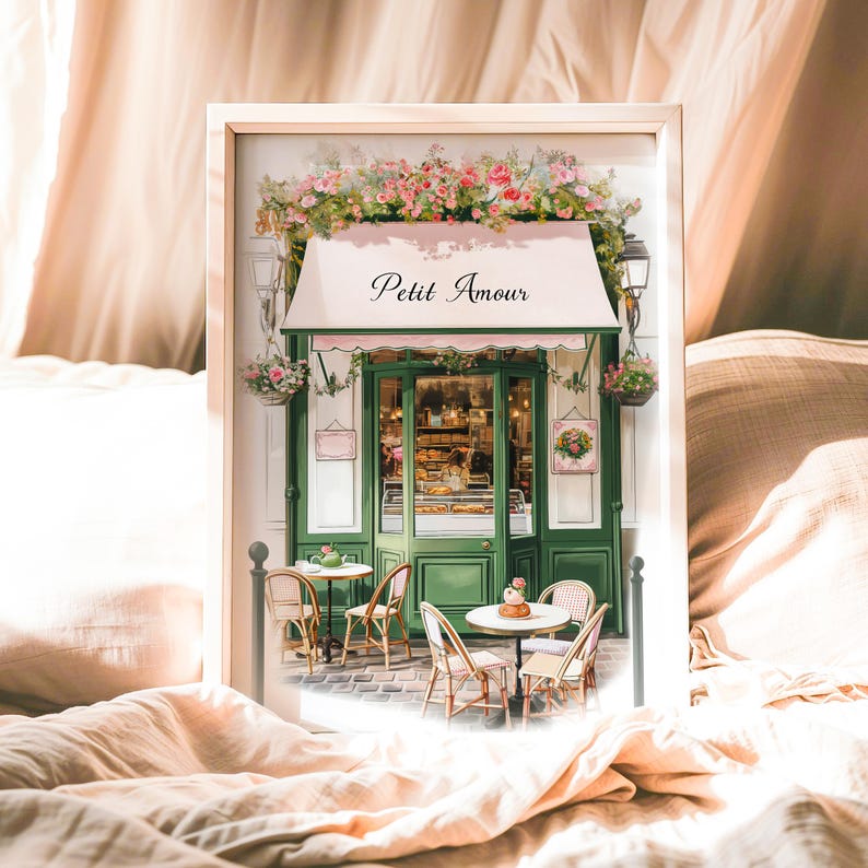 May include: A watercolor painting of a Parisian cafe with a green awning that says "Petit Amour". The cafe has a green door and windows with pastries visible inside. There are two tables with chairs outside the cafe.