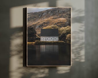 May include: A stone church with a dark green roof sits on a grassy hill overlooking a still body of water. The church is reflected in the water.