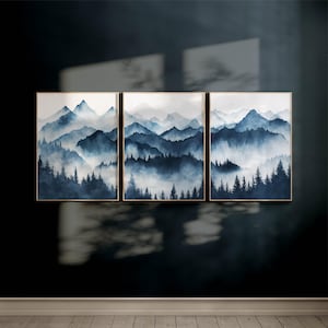 Può includere: Tre dipinti ad acquerello incorniciati di un paesaggio montano nebbioso in tonalità di blu. I dipinti sono disposti orizzontalmente, con il dipinto centrale leggermente più grande dei due ai lati.