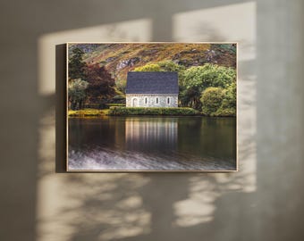 May include: A stone chapel with a dark gray roof sits on a small island in a still lake. The chapel is surrounded by trees and hills. The reflection of the chapel is visible in the water.