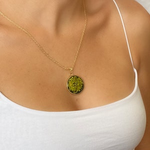 May include: A gold chain necklace with a round pendant featuring a green pressed flower design.