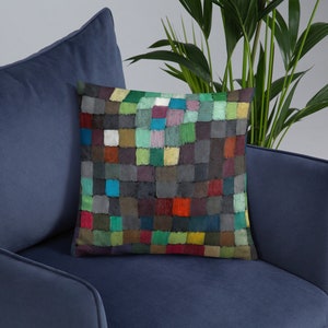 May include: A colorful square patterned throw pillow with a geometric design in shades of green, blue, red, yellow, and brown. The pillow is sitting on a blue couch.