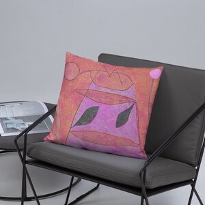 May include: A square throw pillow featuring a vibrant abstract design with a textured orange and pink background. The surface displays dark, thin, hand-drawn lines forming geometric shapes, circles, and two prominent dark green leaf-like motifs.