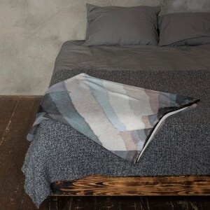 May include: A gray bed with a gray and white striped throw blanket on top. The bed has a wooden frame and is made of a soft, comfortable material.