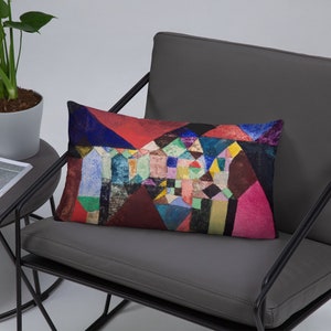 May include: A colorful geometric pillow featuring a painting of abstract shapes in shades of red, blue, green, yellow, and black. The pillow is rectangular and has a soft, plush texture.