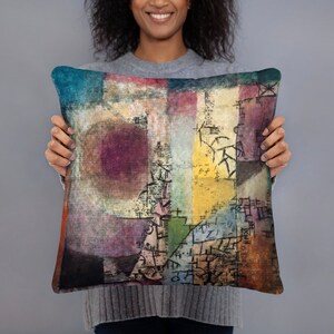 May include: A throw pillow with a colorful abstract design featuring geometric shapes, scribbles, and a large, circular, pink-purple shape in the center. The design is reminiscent of a painting.