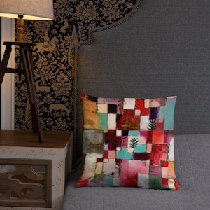 May include: A square throw pillow featuring a grid-like pattern of multicolored rectangular blocks in shades of red, pink, teal, white, and black. The design includes small, stylized green tree illustrations scattered across the surface.