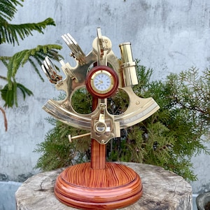 May include: A brass nautical sextant replica with a small clock face, mounted on a wooden base. The sextant features intricate details and a polished finish. The base is a rich, reddish-brown color.