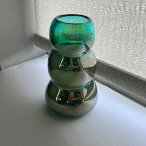 May include: A stack of three round glass vases in shades of green and silver. The vases are stacked on top of each other, with the largest vase at the bottom and the smallest vase at the top.