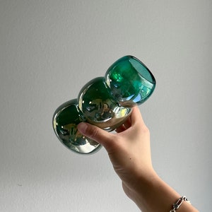 May include: A green glass vase with a unique, bulbous shape. The vase has a metallic sheen and is perfect for displaying flowers or other decorative items.