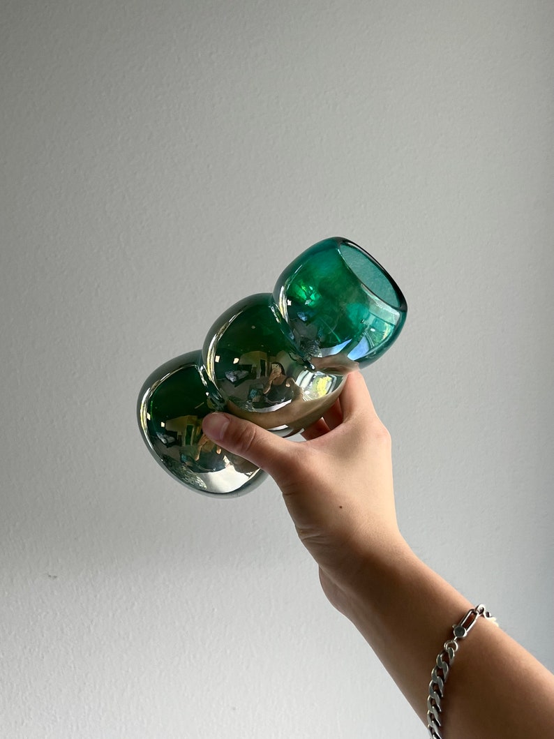 May include: A green glass vase with a unique, bulbous shape. The vase has a metallic sheen and is perfect for displaying flowers or other decorative items.