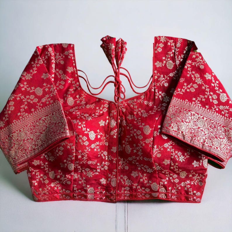 May include: A red brocade blouse with a silver floral pattern and a tie-up back.