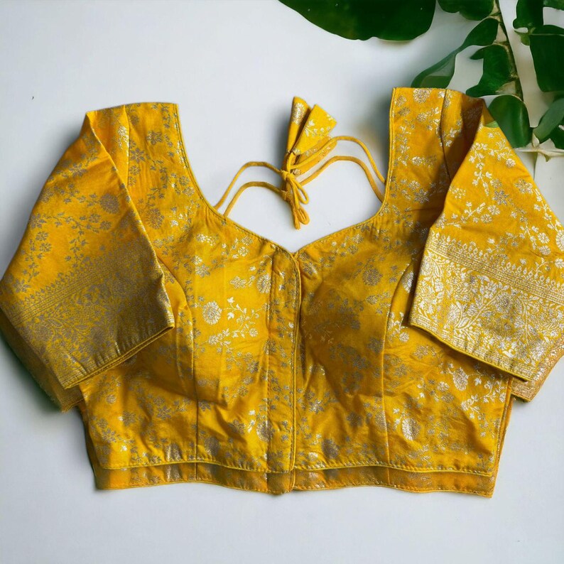 May include: A yellow brocade blouse with silver embroidery and a hook and eye closure. The blouse has short sleeves and a V-neckline.
