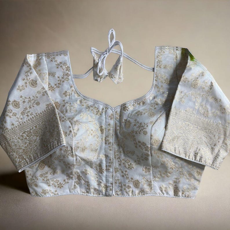 May include: A white brocade blouse with gold floral embroidery and a tie-up back.