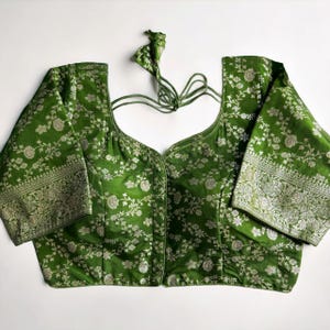 May include: A green brocade blouse with silver floral embroidery and a tie-up back.