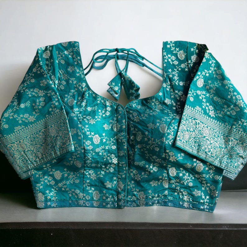 May include: A teal blue brocade blouse with a silver floral pattern and a tie closure at the back.
