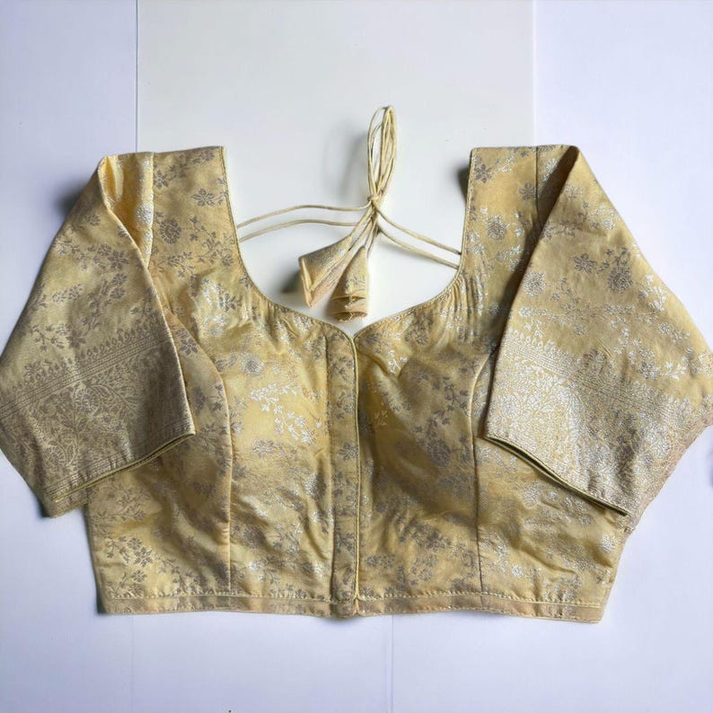 May include: A pale yellow brocade blouse with a silver floral pattern and a tie closure at the back.