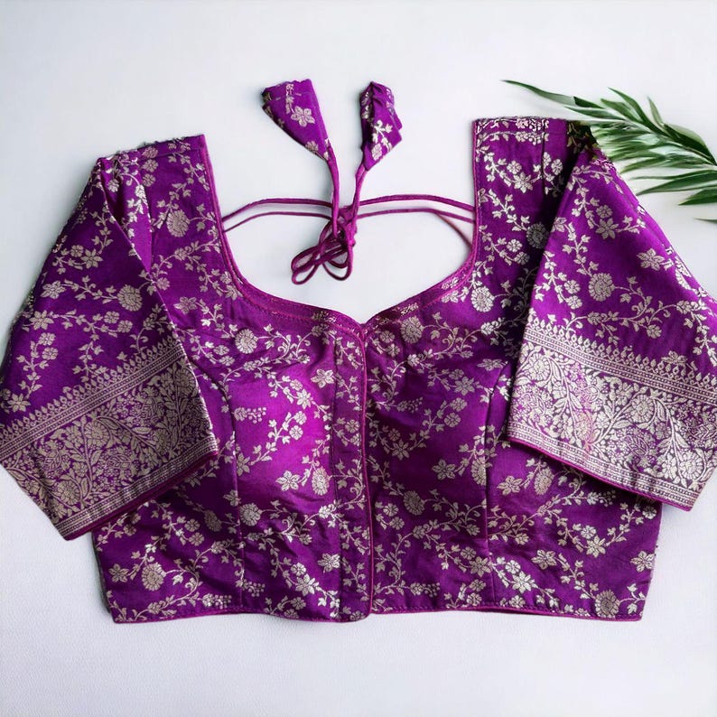 May include: A purple brocade blouse with a floral pattern and silver thread embroidery. The blouse has a scoop neck and short sleeves.