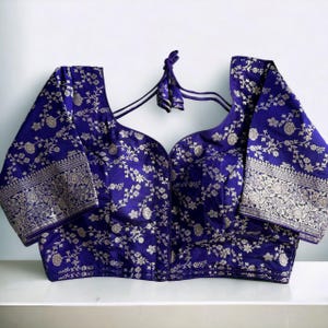 May include: A purple brocade blouse with silver floral embroidery and short sleeves. The blouse has a deep V-neckline and a tie-up back.