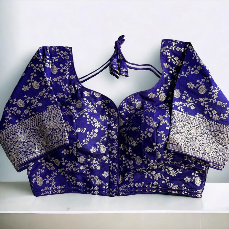 May include: A purple brocade blouse with silver floral embroidery and short sleeves. The blouse has a deep V-neckline and a tie-up back.