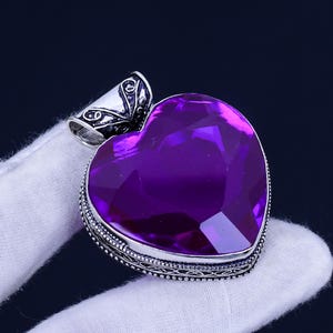 May include: A silver heart-shaped pendant with an ornate design and a large, faceted purple gemstone.