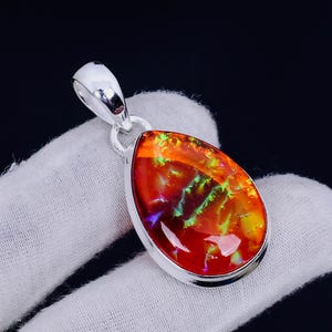 Könnte beinhalten: Ein tropfenförmiger Anhänger mit einem leuchtenden roten, orangefarbenen und grünen Opal-Edelstein, der in Sterlingsilber gefasst ist.