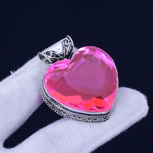 May include: A silver heart-shaped pendant with an ornate design and a pink crystal in the centre.