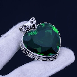May include: A silver heart-shaped pendant with an ornate design and a large, faceted green gemstone.