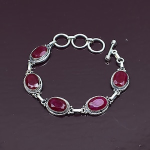 Può includere: Un bracciale in argento con cinque pietre preziose di rubino rosso intenso, di forma ovale e sfaccettate, incastonate in cornici di metallo intrecciato. Il bracciale include una chiusura a T e tre anelli di regolazione circolari.