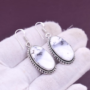 May include: A pair of silver drop earrings. Each earring has an oval white stone with black and grey markings, set in a silver frame with a rope-style edge. The earrings have a hook fastening.