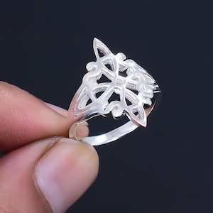 May include: A silver ring featuring a delicate, intricate design. The ring is crafted from a single piece of metal and has a smooth, polished finish.